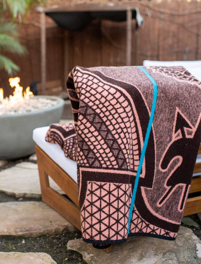 Thula Tula blankets African Basotho blanket in salmon and black color draped over modern wooden outside chair in front of a fire  mobile version