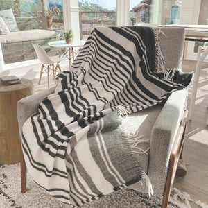 Women tying shoelaces sitting on bed in bedroom sitting on Xhosa Nation wrap, blanket or throw sustainably and ethically made in South Africa. This Xhosa inspired black and white stripe
