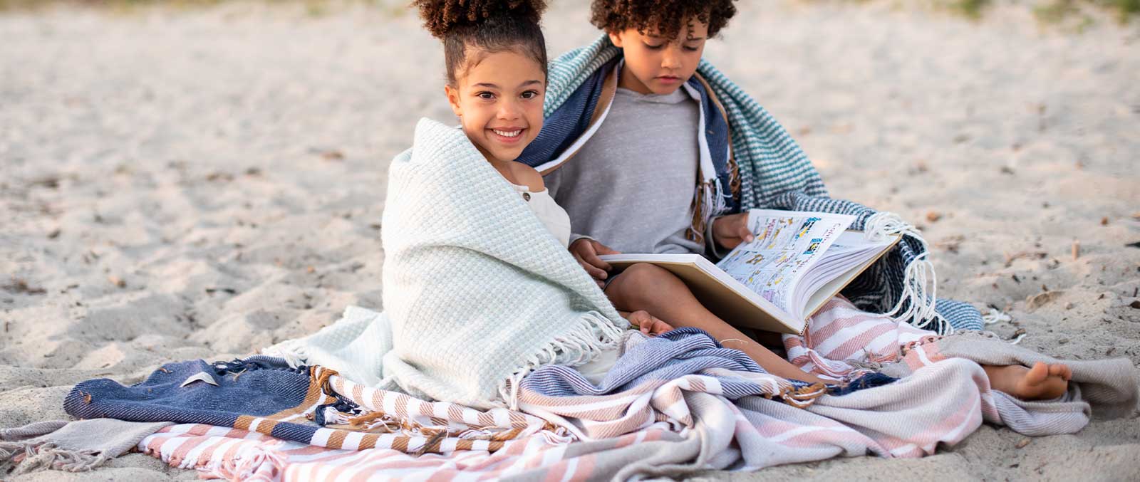 two young children on a beach sitting under african blankets 