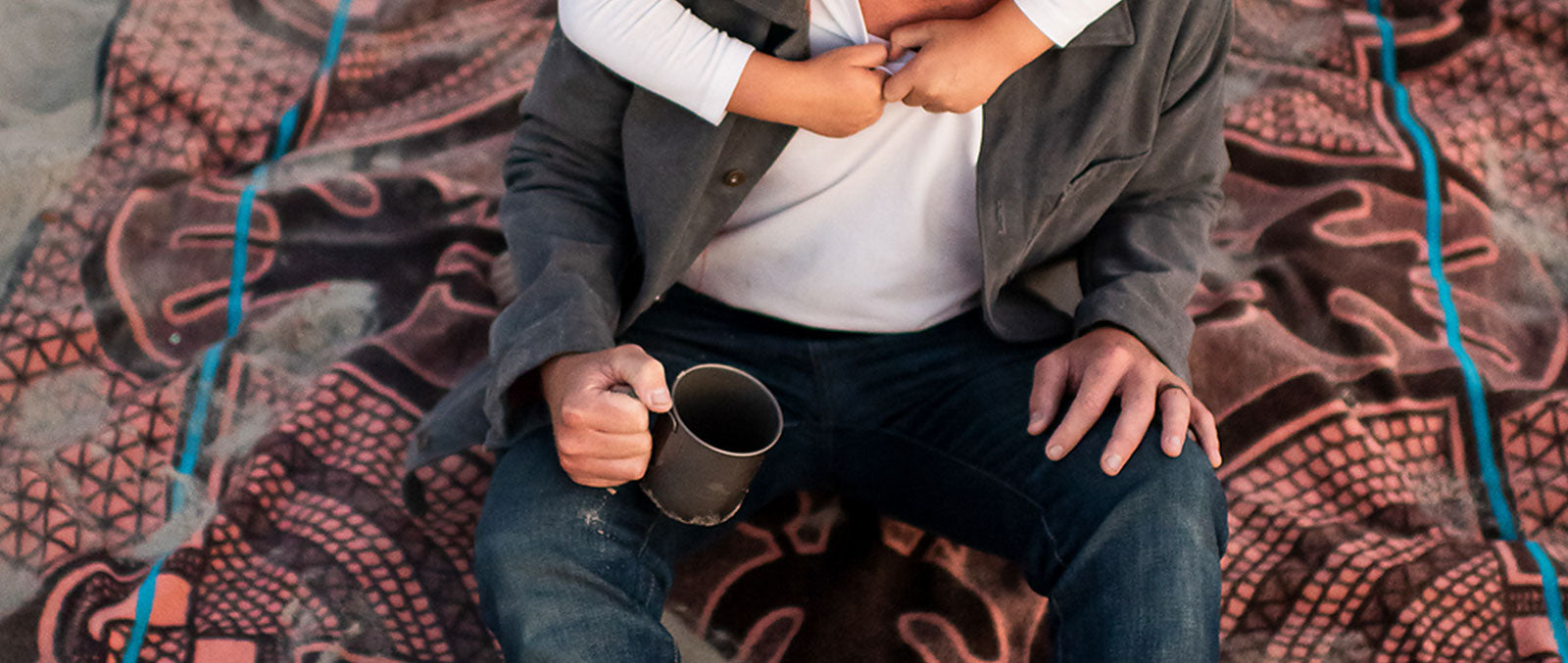 a man is is sitting on the blanket with cup of coffee in the hand