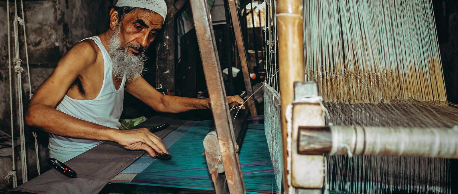 an old man is weaving thread on loom in the past era