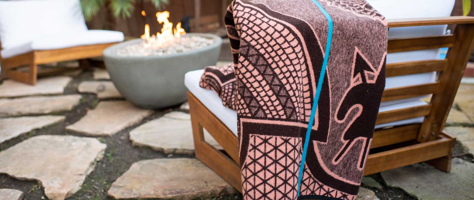 Thula Tula blankets African Basotho blanket in salmon and black color draped over modern wooden outside chair in front of a fire 