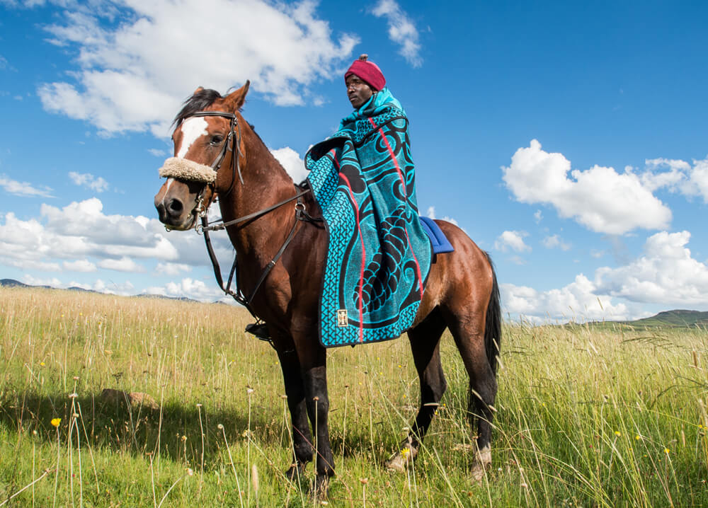 A man is sitting on the horse with wearable blanket
