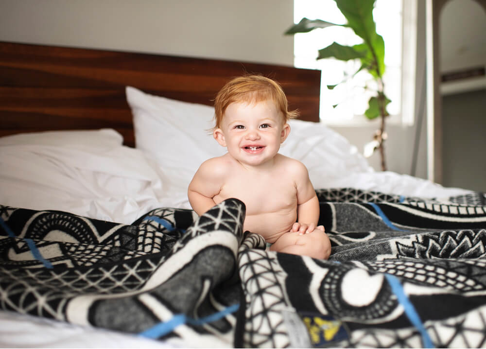 baby sitting on bed with blanket by thula tula