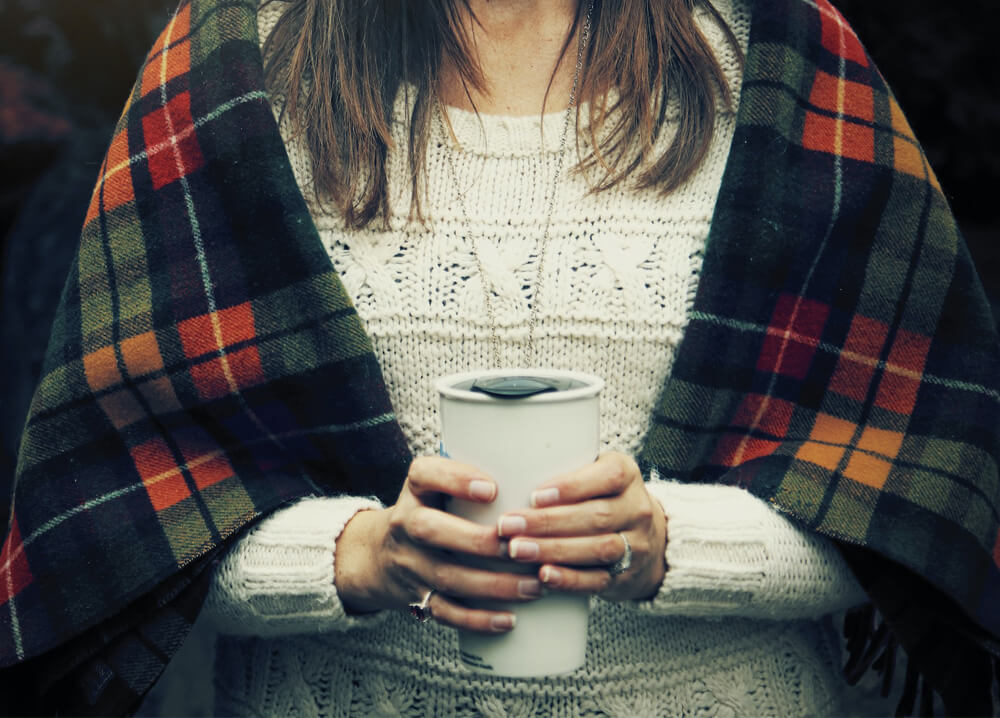 a women has cup in hand and wrapped in fall blanket