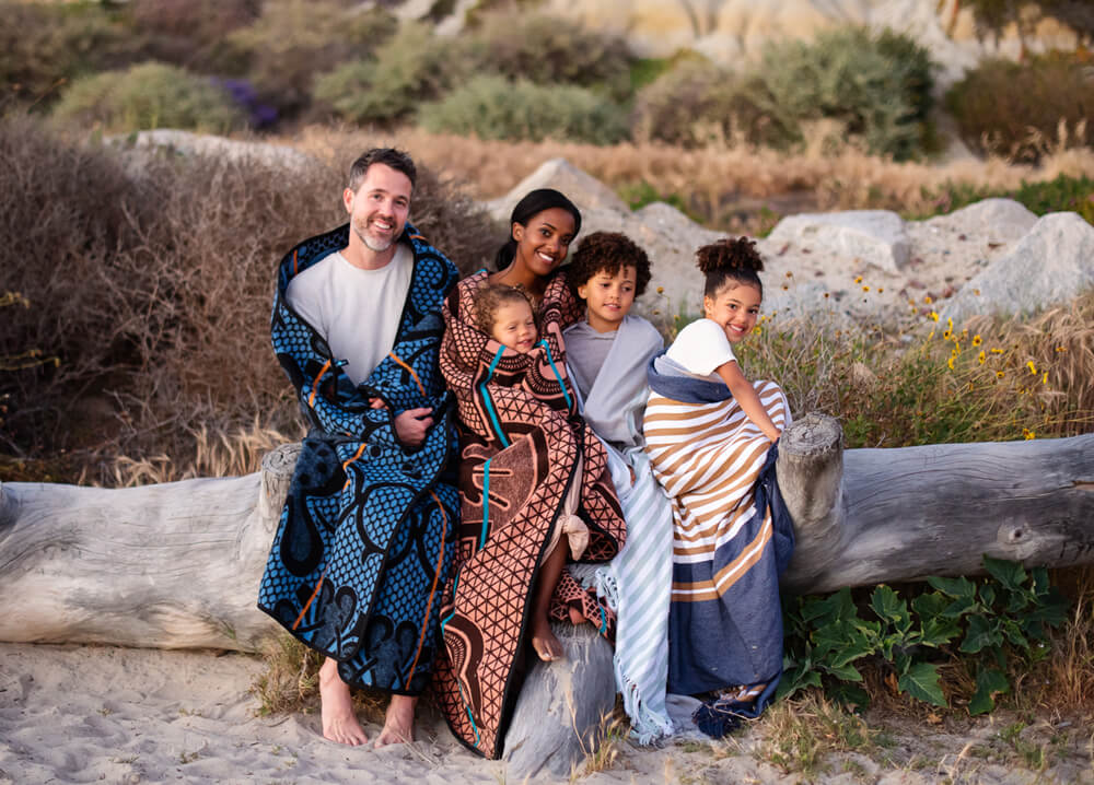 man and women with their kids wrapped in wearable blankets by thula tula