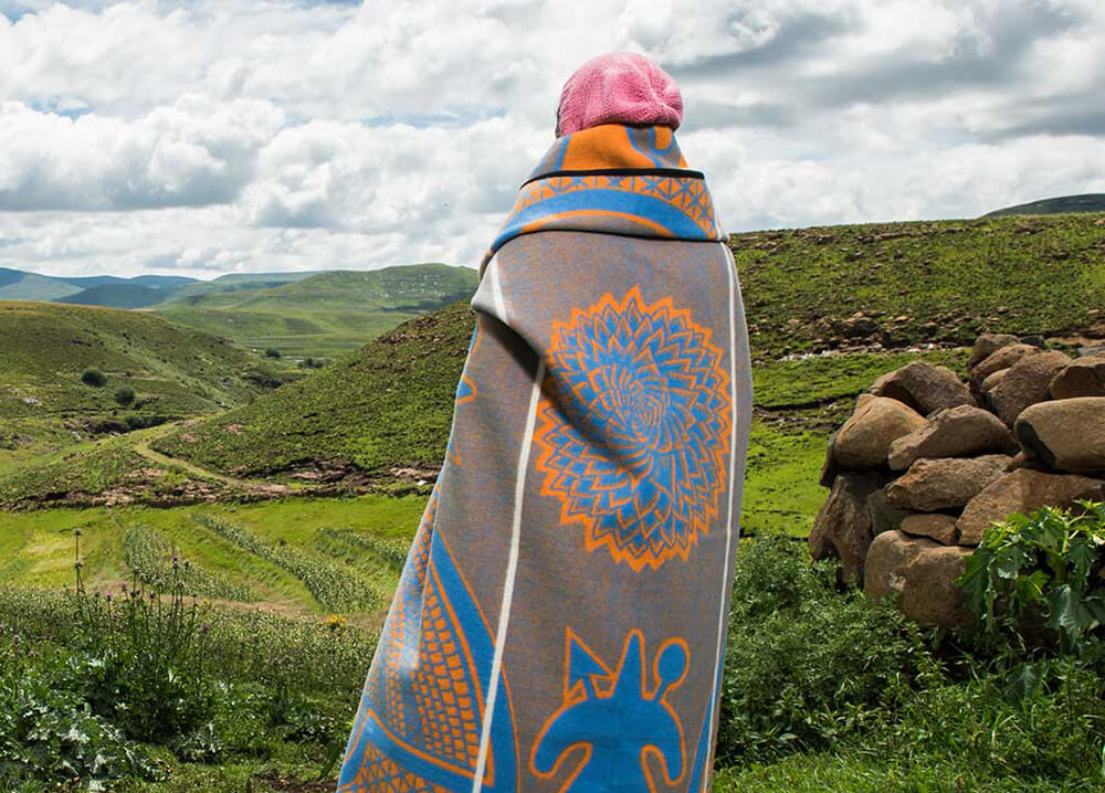 a women is standing on green land wrapped in blanket by thula tula
