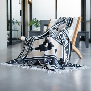 Wild dove colored Ndebele nation inspired wrap, blanket or throw sustainably and ethically made in South Africa incredibly soft, warm, and exceptionally durable blanket draped over folded chair in modern house setting 
