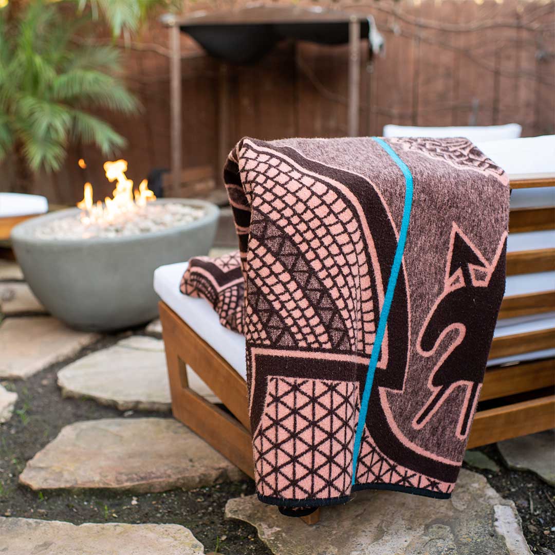 Basotho Heritage blanket and wrap or throw handcrafted in South Africa chromatic Salmon and peacock throw drapped across an outdoor chair in a modern outdoor house garden in front of a fire