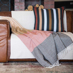 a lyric collection read and black wrap, blanket or throw sustainably and ethically made in South Africa shows the intricate weave and colors draped over beautiful leather couch