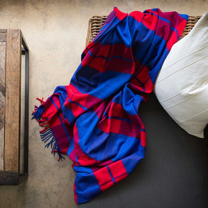 ﻿Maasai Shuka incredibly soft, warm, and exceptionally durable blankets throw in plaid red and royal blue Sustainably and ethically crafted in South Africa lying on a modern styled wicka chair in modern house 