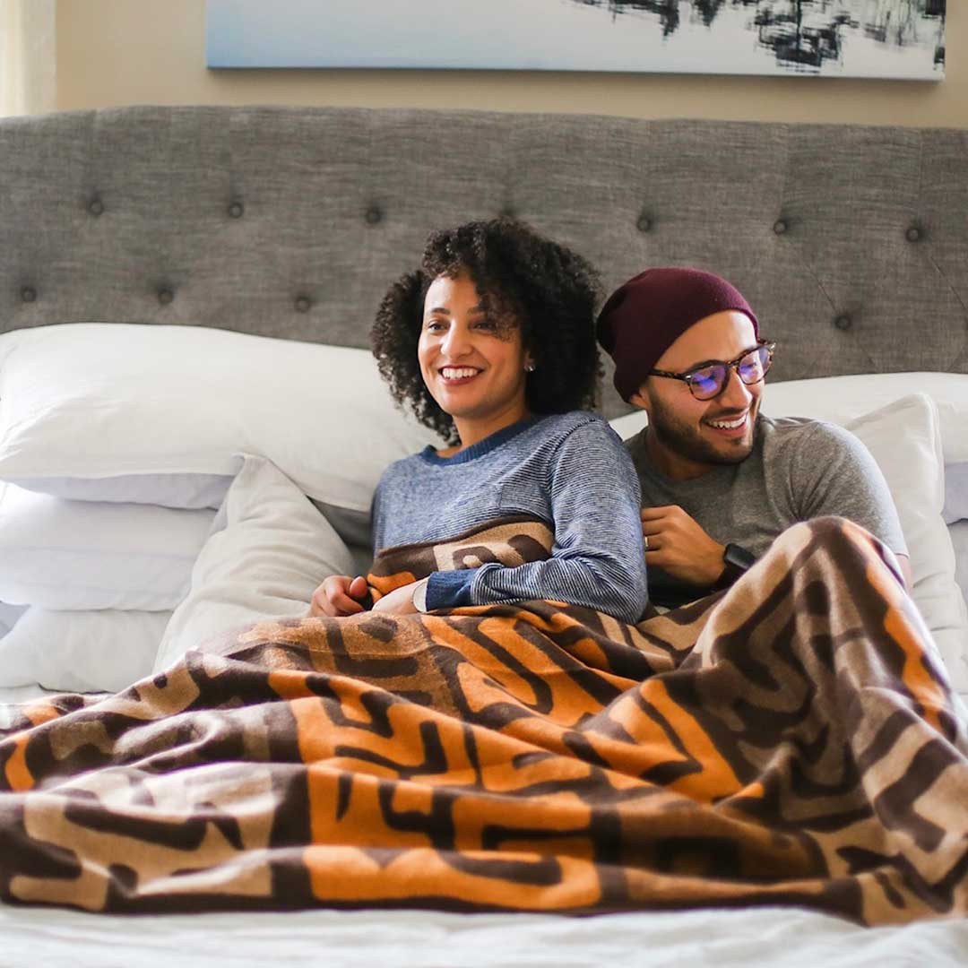 Couple cuddled up and comfy laughing and having fun under soft African inspired designed Congolese kuba cloth wrap or blanket handmade in South Africa 